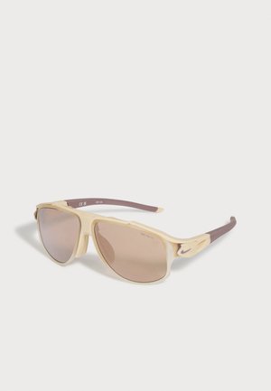 Lunettes de soleil Nike beige et marron avec des verres teintés rectangulaires et un logo visible sur la branche, exposées sur une surface blanche.