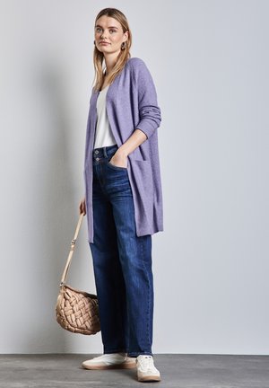 Cardigan long lavande, top blanc, jeans bleu foncé et baskets blanches. Sac tissé beige avec une longue sangle. Textures lisses, coupe décontractée.