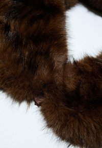 Scarf in pelliccia sintetica marrone con una consistenza morbida e densa, caratterizzato da un nastro di raso liscio come accentuazione a un'estremità. Il design è circolare e soffice.