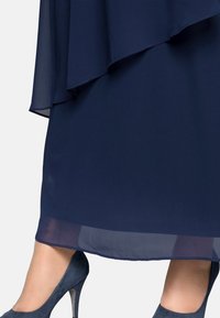 Robe en chiffon marine avec un design superposé, ourlet transparent et talons hauts. Texture lisse et forme fluide allant de la longueur genoux à la cheville.