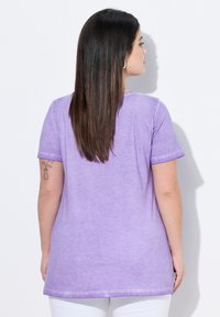 Camiseta de manga corta morada con un corte relajado, cuello redondo y una tela suave y texturizada. La línea del dobladillo llega más allá de las caderas.