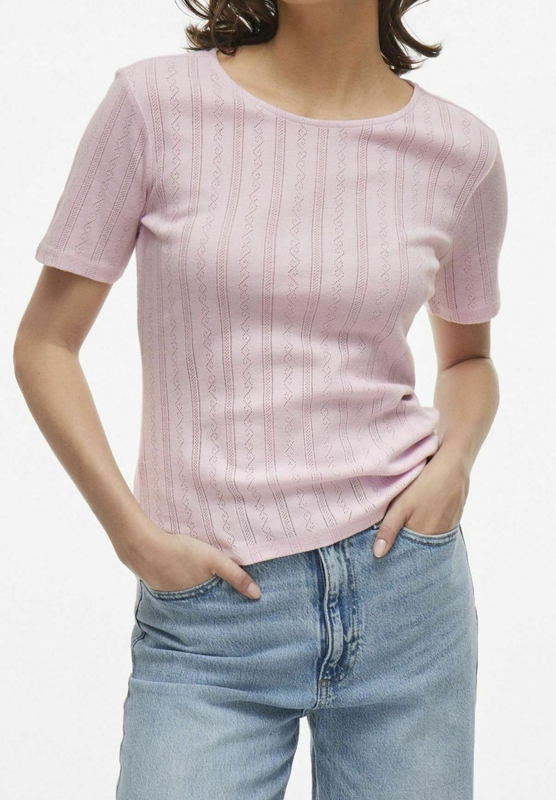 Haut rose à manches courtes avec un motif texturé de rayures verticales. Présente un col rond et une coupe ajustée, associé à un jean en denim bleu.