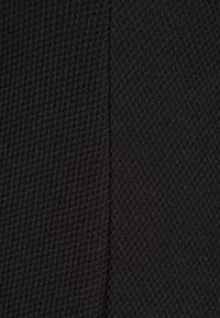 Gros plan sur un tissu noir texturé avec une couture verticale subtile divisant deux motifs de tricot légèrement différents.