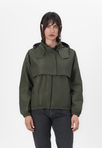 Casaco de chuva verde oliva com capuz, cintura elástica e fecho de correr à frente. Apresenta fechos de pressão nos ombros e é feito de um tecido leve.