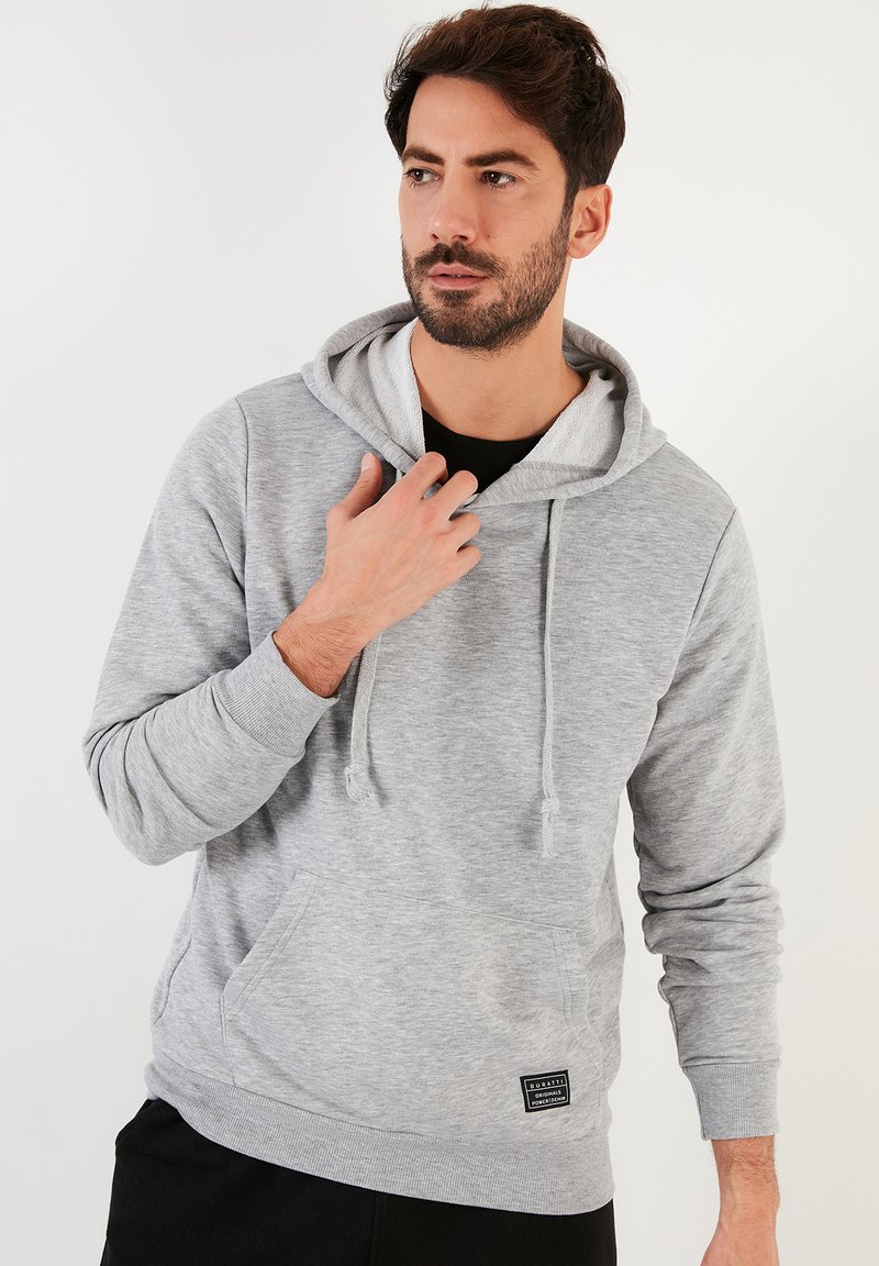 Gray hooded sweatshirt made of soft fabric, featuring a front pocket, drawstrings, and a logo patch at the bottom.