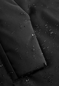 Tessuto impermeabile nero con superficie testurizzata, che mostra gocce d'acqua che si formano sulla materia. Presenta cuciture lisce e un bordo ripiegato.