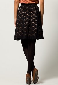 Svart spetskjol med elastiskt midjeband, som har en mjukt svängande design och halvgenomskinliga detaljer ovanpå en solid foder, kombinerad med strumpbyxor och klackskor.