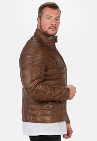 Bruine leren jas met een quiltpatroon, hoge kraag, zijzakken en ritssluiting, met een gestructureerde afwerking en een getailleerd ontwerp.