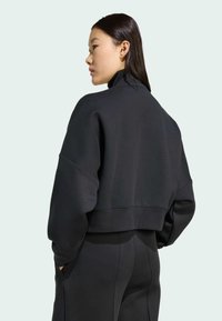 Zwarte cropped sweatshirt met een hoge kraag, zachte textuur en verlaagde schouders, gecombineerd met bijpassende broek, gezien vanuit de achterkant.