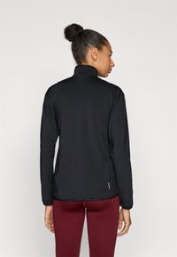 Fekete hosszú ujjú dzseki magas gallérral, rugalmas anyagból, karcsúsított szabással. Enyhén fényes, finom márkajelzéssel a szegély közelében.