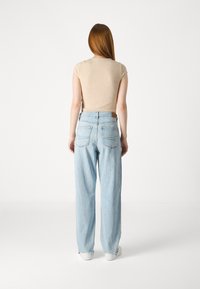 Jean large bleu clair avec un ourlet effiloché, deux poches arrière, associés à un t-shirt beige ajusté en côte. Design simple et décontracté.