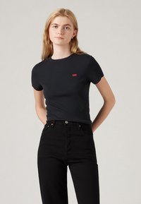 Svart kortermet T-skjorte i ribbet stoff, med en liten rød Levi's-logo på brystet, kombinert med høytlivs svarte jeans.