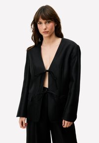 Zwarte blazer met een diepe V-hals en strikjes aan de voorkant. Gemaakt van een gladde stof, met vier zakken en een gestructureerde vorm.