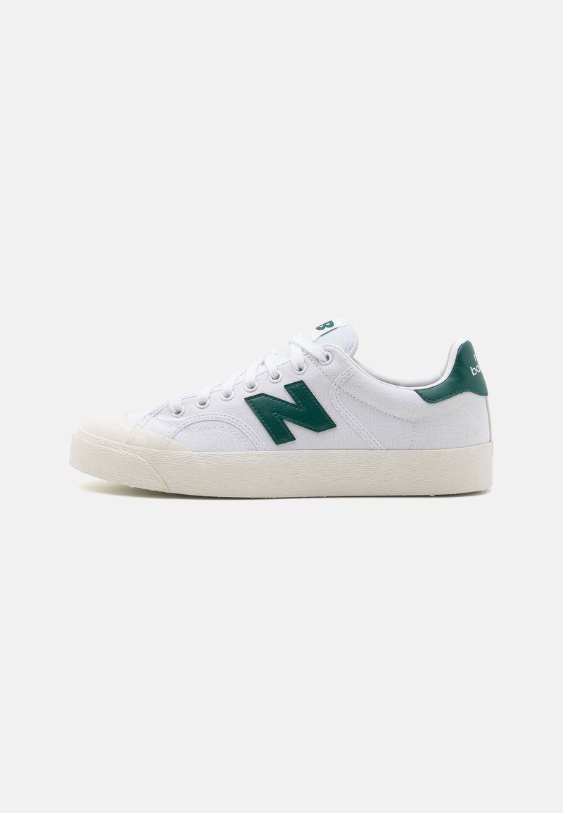 Zapatilla de lona blanca con una lengüeta de cuero verde en el talón y un logotipo 'N' de gran tamaño. Punta redondeada, diseño con cordones y suela de goma.