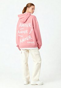 Felpa oversized rosa con la scritta "AMOUR" in bianco sulla schiena. Abbinata a pantaloni cargo beige chiaro e sneakers bianche con plateau.