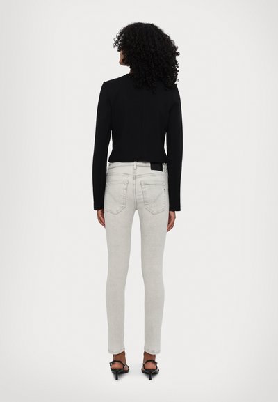 Czarna dopasowana krótka kurtka z długimi rękawami, zestawiona z jasnoszarymi obcisłymi dżinsami z tylnymi kieszeniami i małą naszywką z logo. Czarne sandały na obcasie.