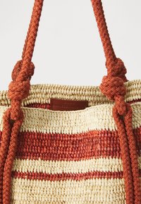 Spleciona torba ze słomy w czerwono-kremowe paski, z skórzaną metką z napisem "Vanessa Bruno" i zawiązanymi czerwonymi, plecionymi uchwytami.