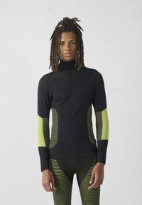 Top atletico nero con collo alto, caratterizzato da accenti a righe verdi sulle maniche. Realizzato in materiale elastico e traspirante per il massimo comfort.