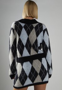Fuzzy sweaterkjole med et argyle mønster i lyseblå, beige og sort. Kort længde med en tætsiddende talje og lange ærmer.