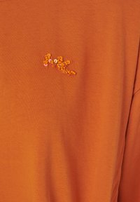 T-shirt di cotone arancione con maniche corte e un dettaglio di paillettes arancioni testurizzate nella parte anteriore, caratterizzata da una superficie di tessuto liscia e uniforme.