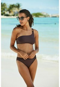 Top bikini marrone a spalla unica con chiusura laterale, abbinato a un fondo a vita bassa con anello laterale decorativo. Texture liscia.
