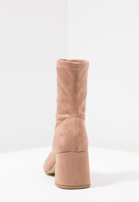Bottine en daim rose clair avec une texture lisse, un bout carré et un talon bloc épais. Présente un détail de couture au dos.
