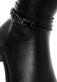 Black ankle boot with a smooth leather texture, featuring a decorative strap and buckle accent, and a low stacked heel.