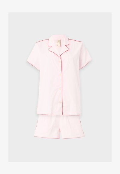 Haut de pyjama à manches courtes rose clair avec boutons et short assorti avec un liseré rouge le long des bords, présenté sur un fond uni.