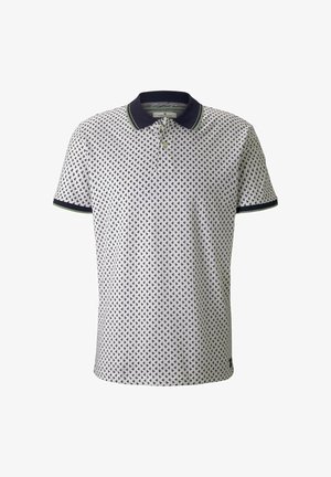 Polo blanc à manches courtes avec un petit motif d’ancre bleu marine, col bleu marine, deux boutons et poignets bleu marine avec bordure verte.