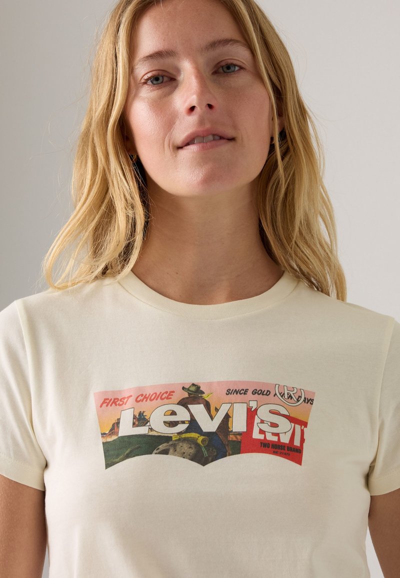 Cremfarbene Baumwoll-T-Shirt mit einem bunten, vintage Levi's Grafikdruck, mit kurzen Ärmeln und einem rundem Ausschnitt.