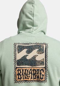 Zelená mikina s kapucňou s textúrovaným vlnovým vzorom a nápisom "Billabong" v štylizovanom písme na chrbte.