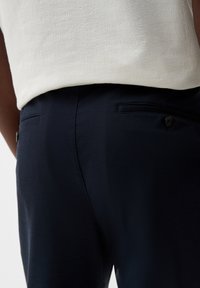 Marineblauwe broek van gestructureerde stof, met twee achterzakken met knoopsluitingen en een gladde tailleband.