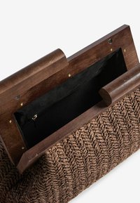 Borsa a mano intrecciata marrone con un corpo texturizzato, telaio in legno e interno in tessuto nero con una tasca con zip.