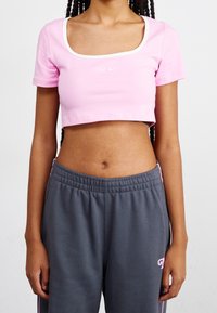 Rosa kortärmad t-shirt med fyrkantig halsringning och vit kant, med en liten vit Nike-logotyp. I kombination med grå joggers med elastisk midja.