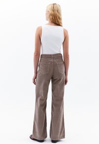 Bruine corduroy broek met wijde pijpen en verticale ribbels, hoge taille en twee achterzakken, gecombineerd met een aansluitend wit tanktop.