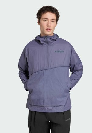 Veste légère violette en tissu texturé, dotée d'une capuche, d'une poche avant et d'un détail de logo vert.