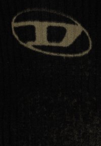 Tissu tricoté noir avec un logo ovale gris proéminent et une lettre "D" stylisée au centre. La texture est légèrement côtelée.