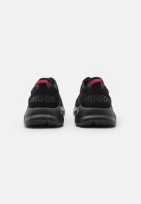 Chaussures de sport noires avec accents rouges. Dotées d'une tige en mesh et synthétique, d'un col rembourré, et d'un marquage "HUGO" bien visible sur le talon.