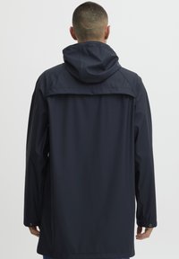 Marine vanntett jakke med hette, preget av en jevn tekstur, lange ermer og knappelukking ved håndleddene. Bakvinduet viser et enkelt design.