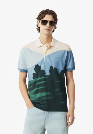 Polo in tonal blu, crema e verde con una stampa paesaggistica di montagne e alberi. Maniche corte e design colletto classico.