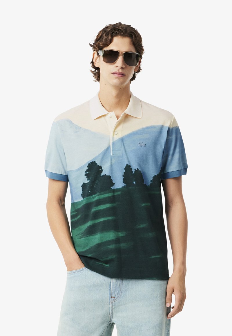 Pikepaita sinisen, kermaisen ja vihreän sävyissä, jossa on maisemakuva vuorista ja puista. Lyhyet hihat ja klassinen kaulustyyli.