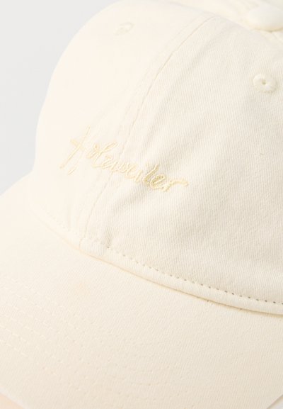 Ecru bawełniana czapka bejsbolowa z małym haftowanym logo "H:Traveller" na przednim panelu, widoczne detale szwów oraz zakrzywiony daszek.