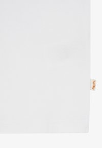 Surface en tissu blanc avec une petite étiquette beige sur le bord droit portant l'inscription "BLK MTS" en lettres orange.