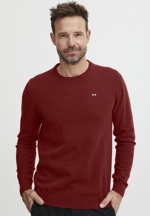 Bordeaux trui van zacht materiaal, ronde hals, geribbelde manchetten en onderzoom, met een klein logo met rode, witte en blauwe strepen op de borst.