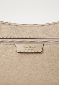 Borsa a mano in pelle beige con finitura testurizzata, dotata di una cerniera in tonalità oro e di una placca con il logo che recita "kate spade NEW YORK."