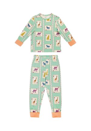 Junges Mädchen steht barfuß in mintgrünen Schlafanzügen mit bunten Tier-Spielkartenmustern in einem hellen, gemütlichen Raum.