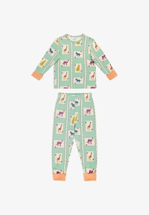 Ragazza giovane in piedi a piedi nudi con pigiama verde menta stampato con carte da gioco di animali colorati in una stanza luminosa e accogliente.