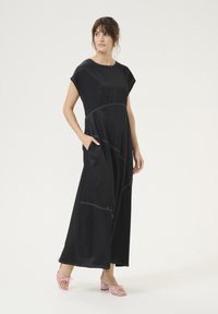 Mustaline kleit lühikeste varrukatega, millel on kontrastsed valged õmblused ja küljetaskud, kantud roosade rihmadega kontsakingadega. Sile tekstuur.