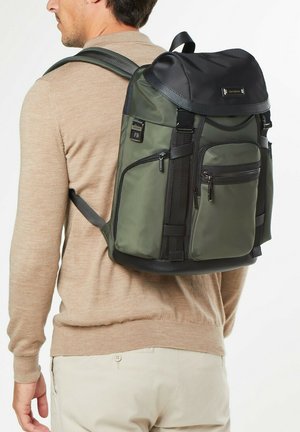 Olivgrüner Rucksack mit schwarzen Akzenten, mehreren Reißverschlusstaschen, gepolsterten Trägern und einem Kordelzugverschluss, der für Komfort und Funktionalität ausgelegt ist.