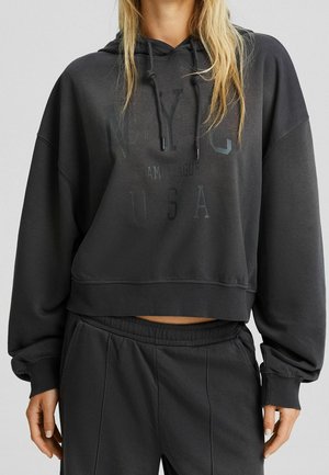 Haut noir coupé avec cordons, arborant l'imprimé "NYC USA". Matière douce, coupe décontractée et détails de bord côtelé. Associé avec un pantalon assorti.